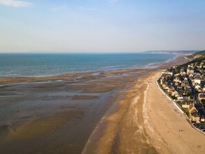 Eine Vogelperspektive einer Küstenstadt mit breitem Strand, Häusern entlang der Küste und freier Sicht auf das Meer.