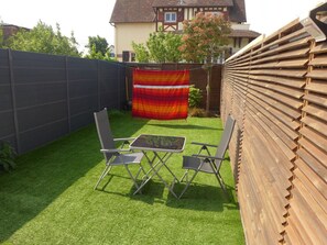 Ein Garten mit Kunstrasen, zwei Metallstühlen und einem Tisch.