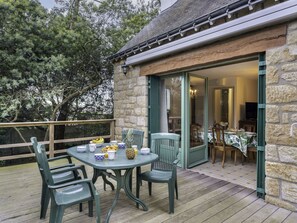 Un espace de restauration en plein air avec une table dressée pour quatre personnes, entourée de chaises, et une vue sur l’intérieur à travers une porte vitrée.