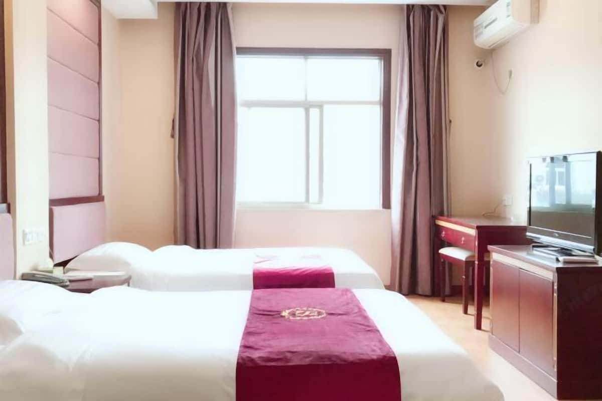 A hotel room with two beds, a desk, a television, and a window with curtains.
