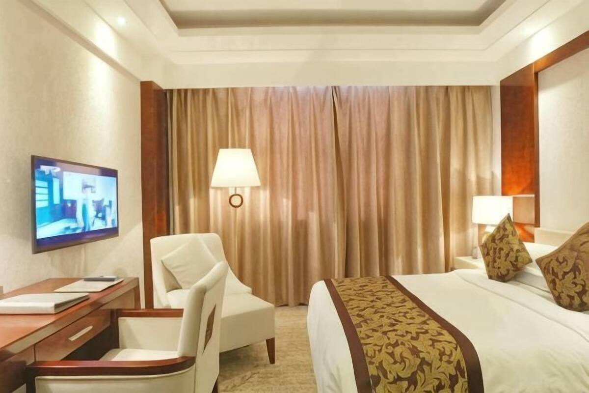 A hotel room with a bed, a desk with a chair, a television, and a lamp.