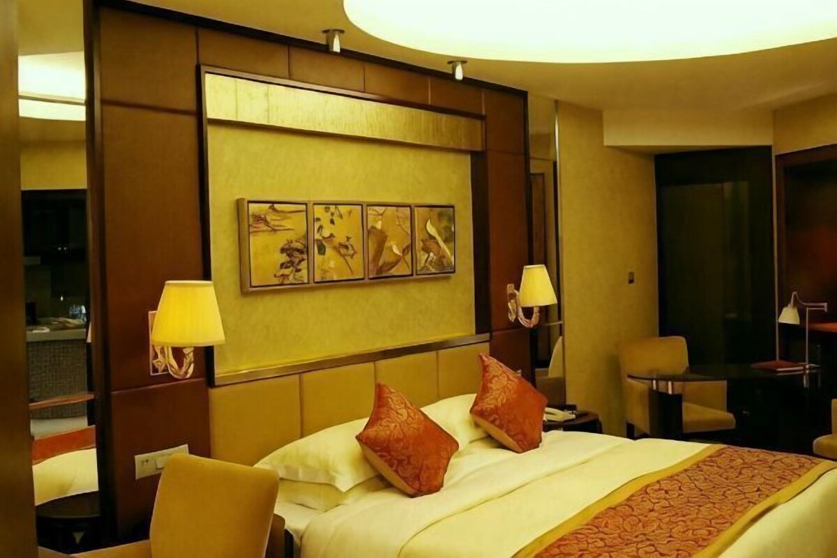 A hotel room with a large bed, two bedside lamps, a headboard with artwork, and a chair.