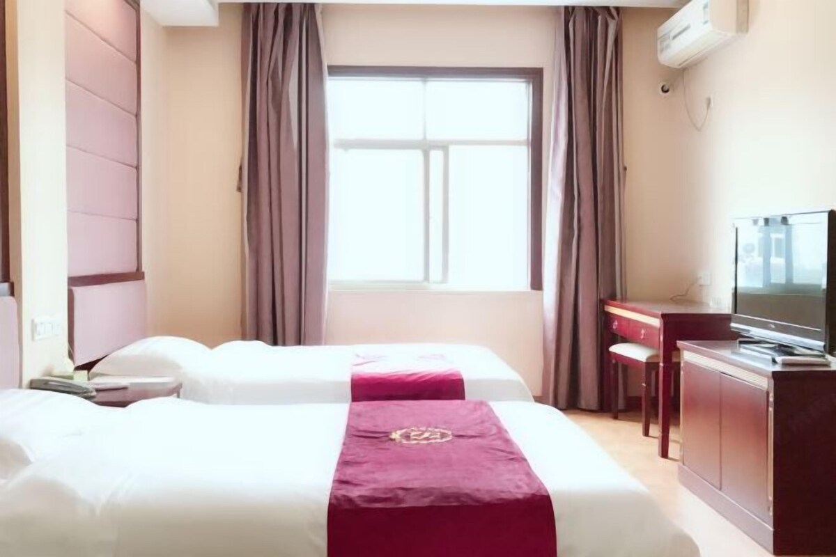 Una habitación de hotel con dos camas, un escritorio, un televisor y una ventana con cortinas.