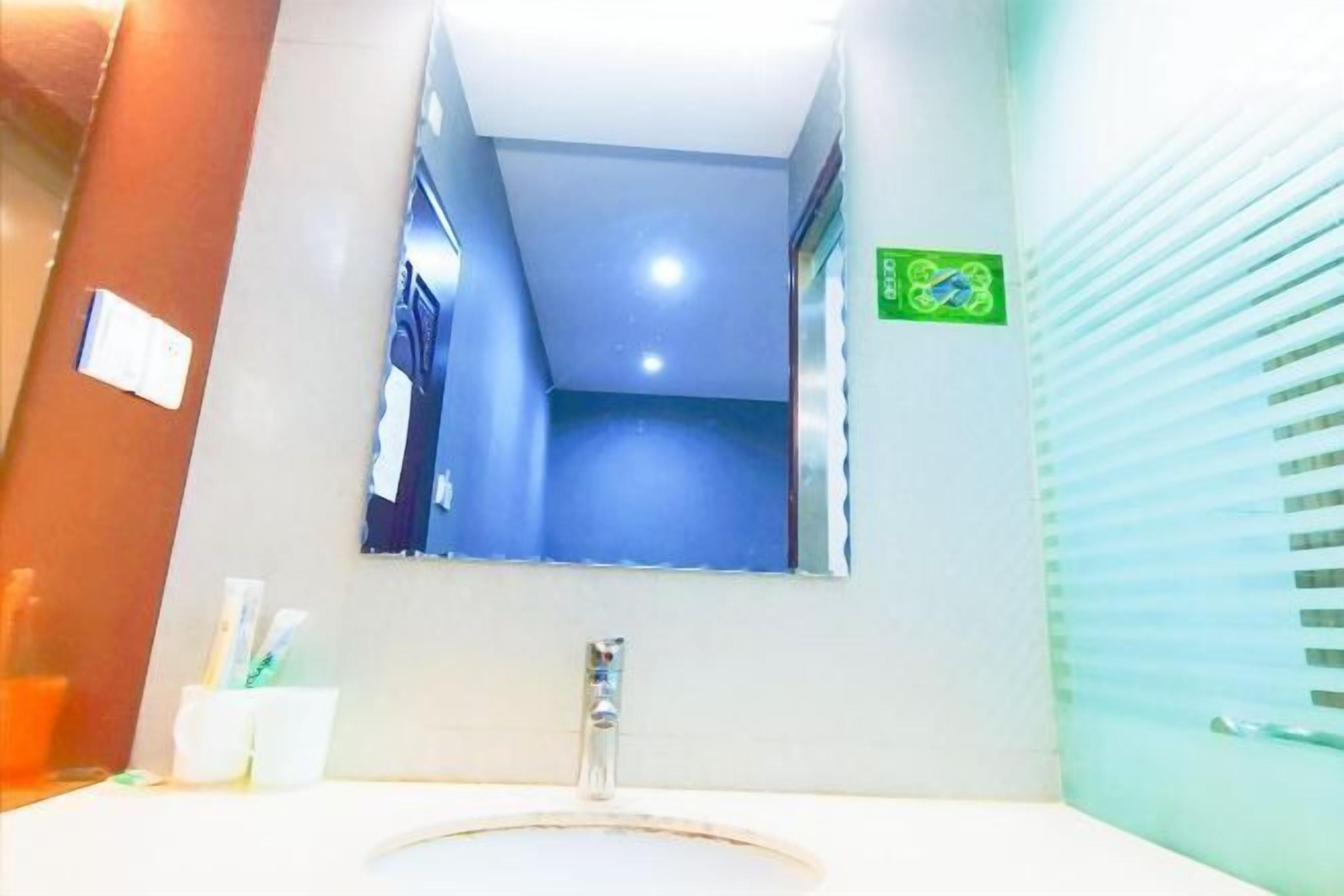 A bathroom with a sink, mirror, and a green sign on the wall.
