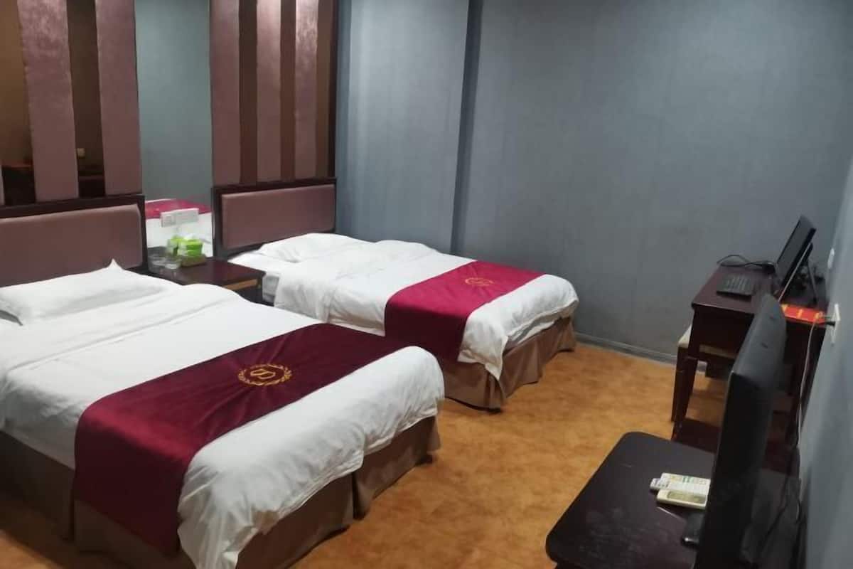 A hotel room with two beds, a desk, and a television.