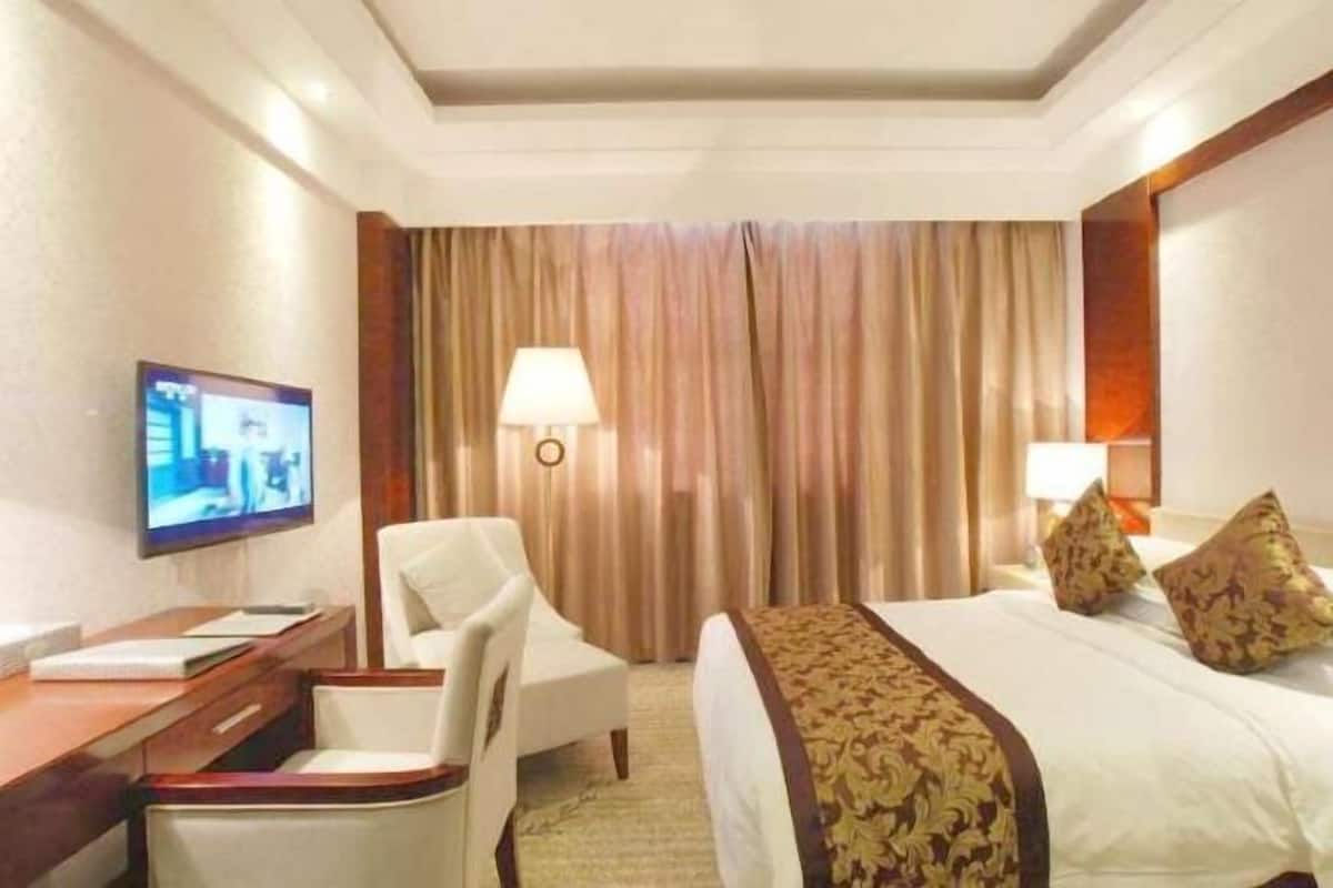 A hotel room with a bed, a desk, a chair, a television, and a window with curtains.