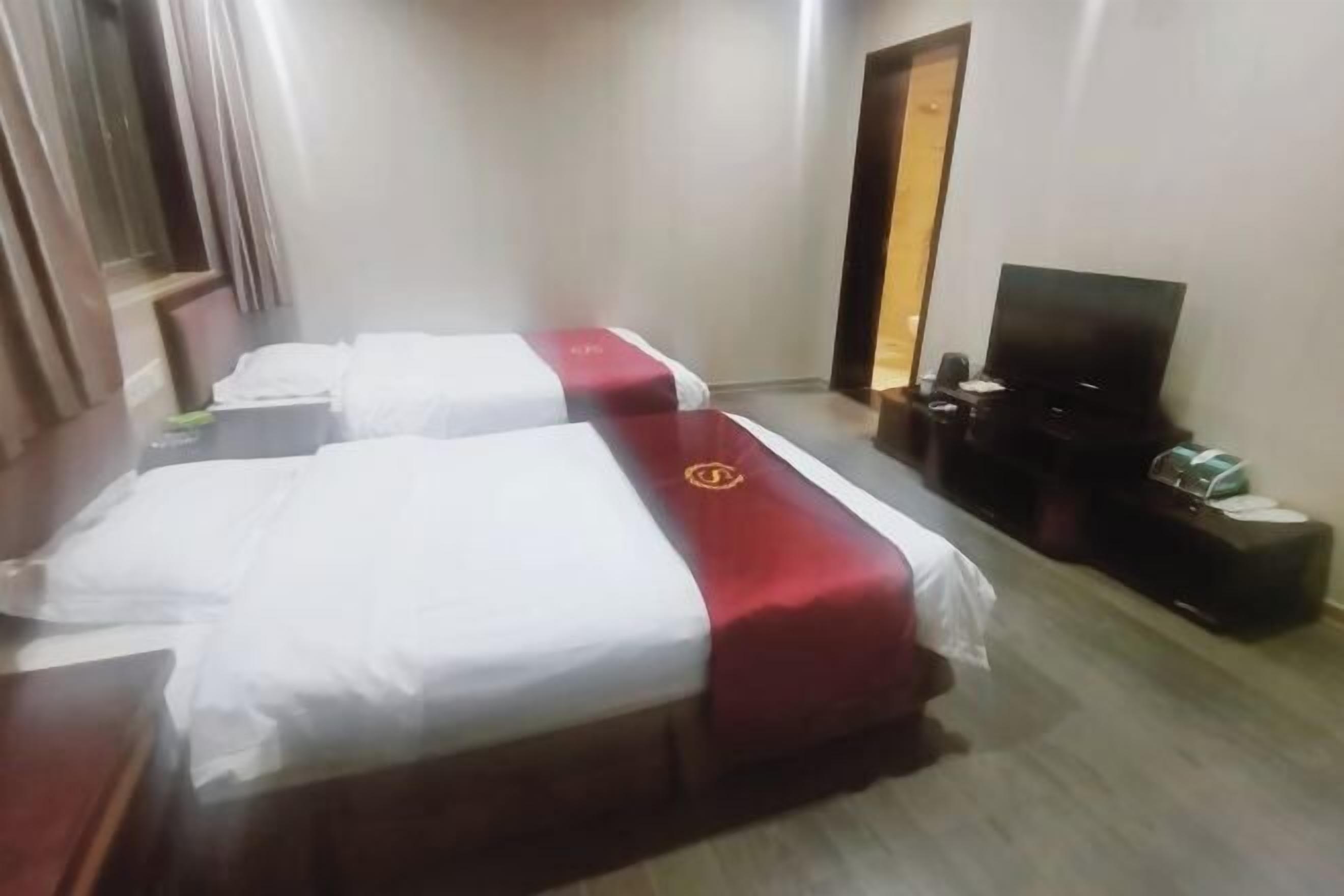 A hotel room with two beds, a TV, and a wooden floor.