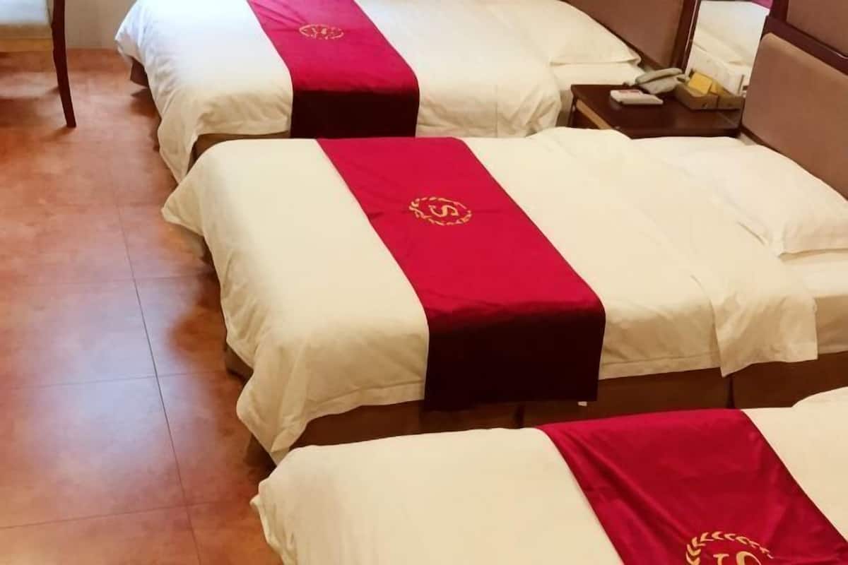 A hotel room with four beds, each with a red and white bedspread and a gold emblem.