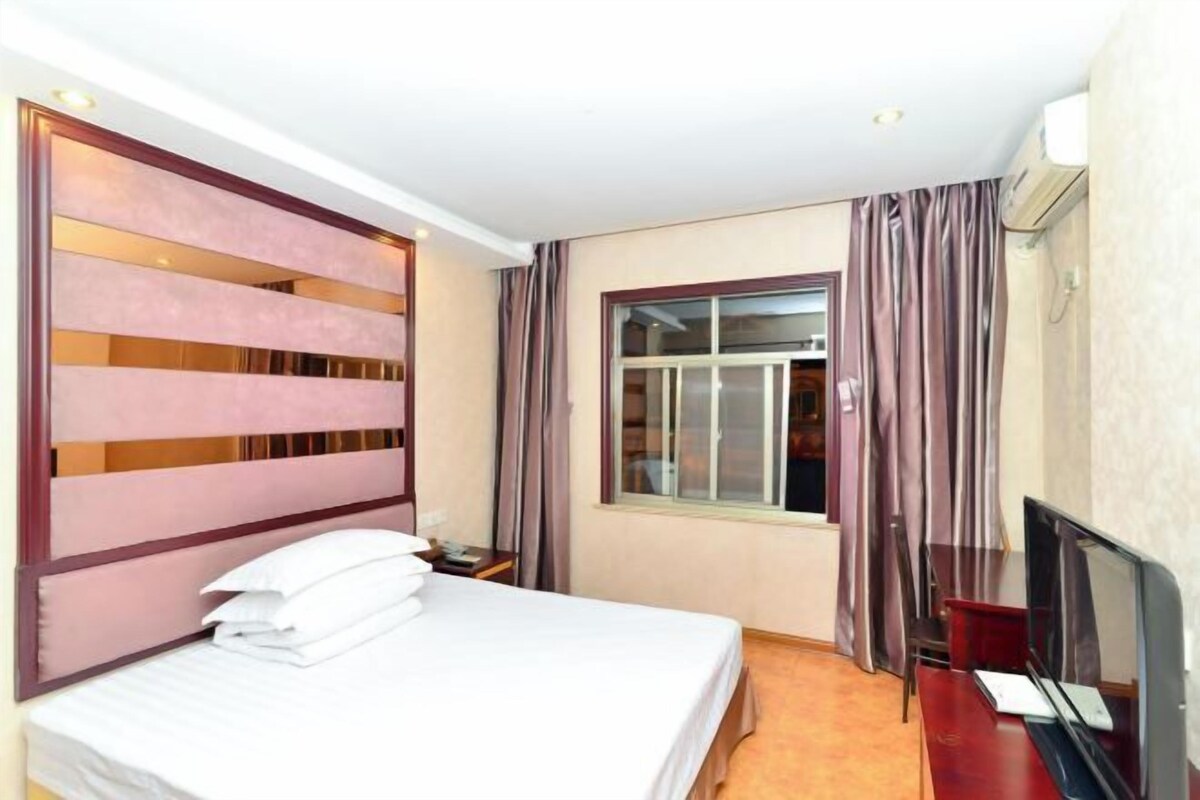 A hotel room with a bed, a desk, a television, and a window with curtains.