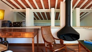 Een kamer met een houten tafel, een stoel, een zwarte schoorsteen en een raam met witte balken.