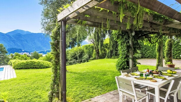 Een overdekt terras met een eettafel, omgeven door weelderige begroeiing en uitzicht op bergen.