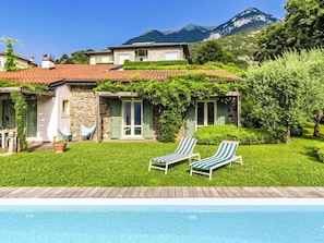 A house with a swimming pool, green lawn, and mountains in the background.