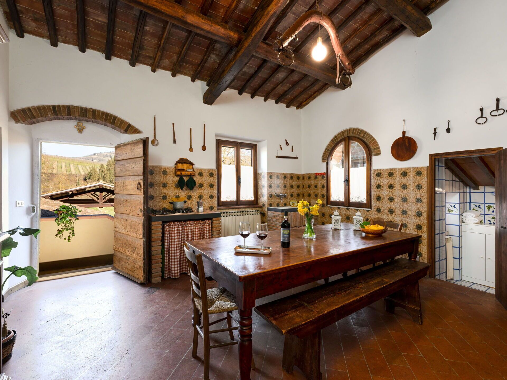 Une cuisine rustique avec une table en bois, un banc et des ustensiles de cuisine suspendus.