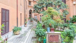 A narrow alleyway with a small garden area, potted plants, and a water spigot.