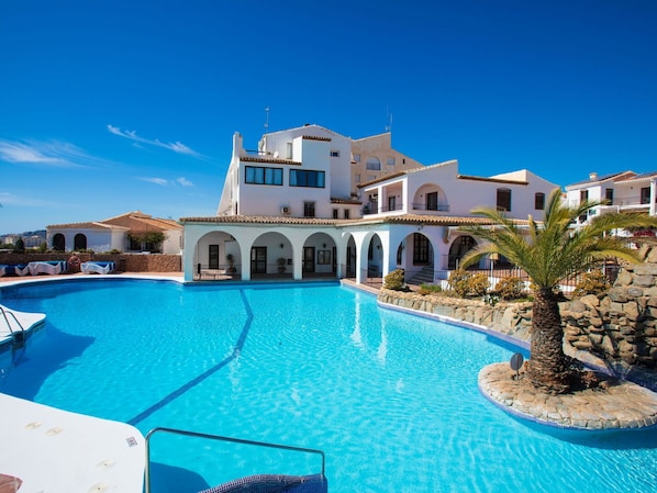 A large swimming pool surrounded by white buildings with multiple arches and balconies.