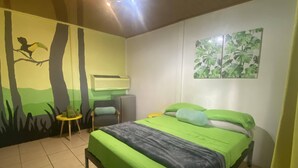 Una stanza con un letto, una sedia, un tavolino, un condizionatore d'aria e un murale a tema naturalistico.