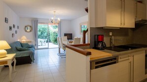 Een moderne keuken met witte kasten, een vaatwasser en een koffiezetapparaat. Er is een eethoek met een tafel en stoelen, en een bank in de woonkamer.