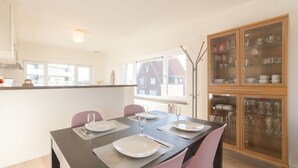 Comedor con mesa preparada para cuatro personas, dos sillas y un aparador de vidrio con vajilla y cristalería.
