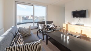 Una sala de estar moderna con un sofá, sillones, una mesa de centro y un televisor de pantalla plana.