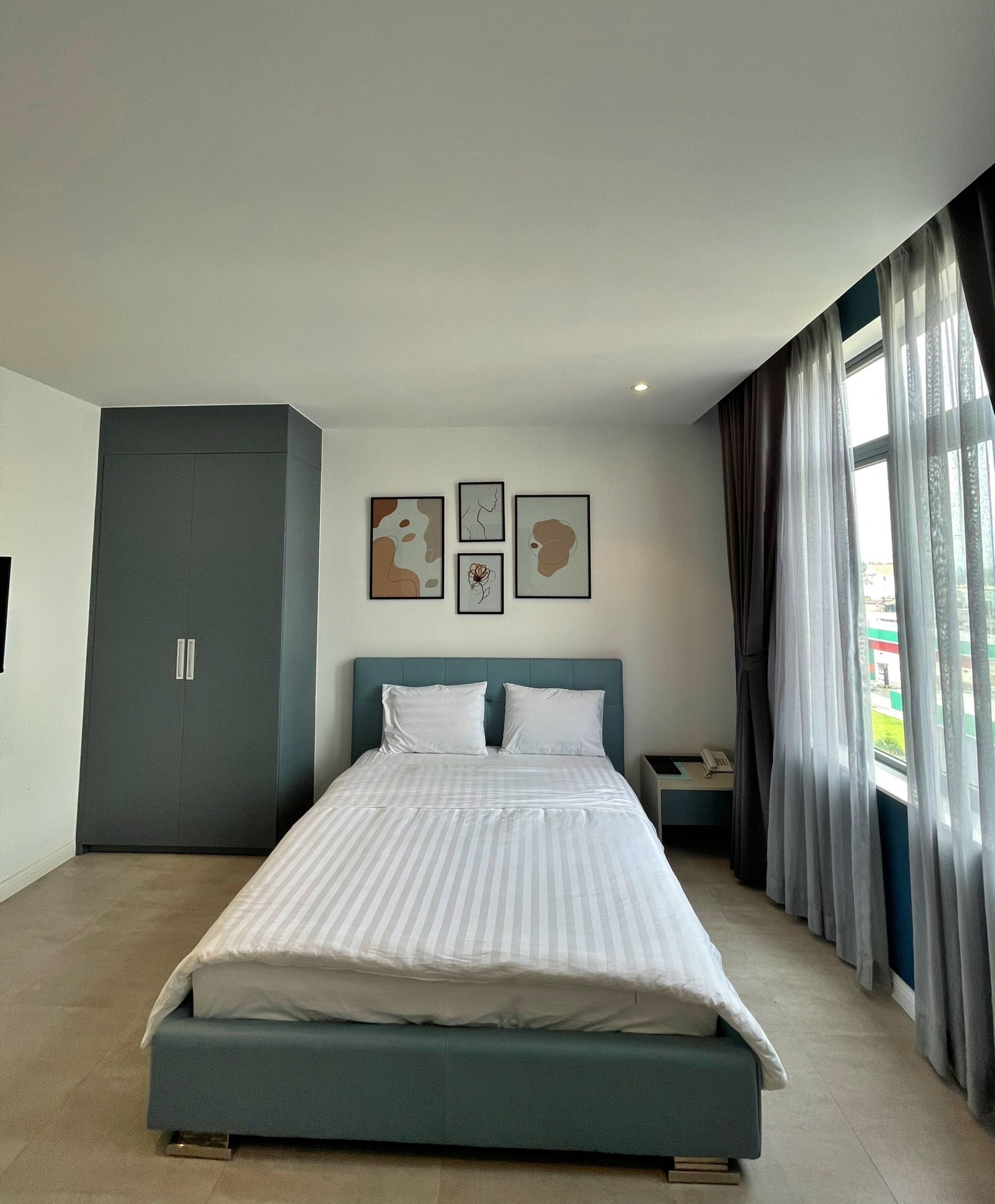 A modern bedroom with a large bed, a wardrobe, and a nightstand. There are three framed artworks on the wall.