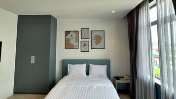 A modern bedroom with a large bed, a wardrobe, and a nightstand. There are three framed artworks on the wall.