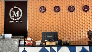 Zona de recepción de un hotel con un mostrador de recepción, un reloj de pared que muestra diferentes husos horarios y un letrero que indica la zona de recepción.