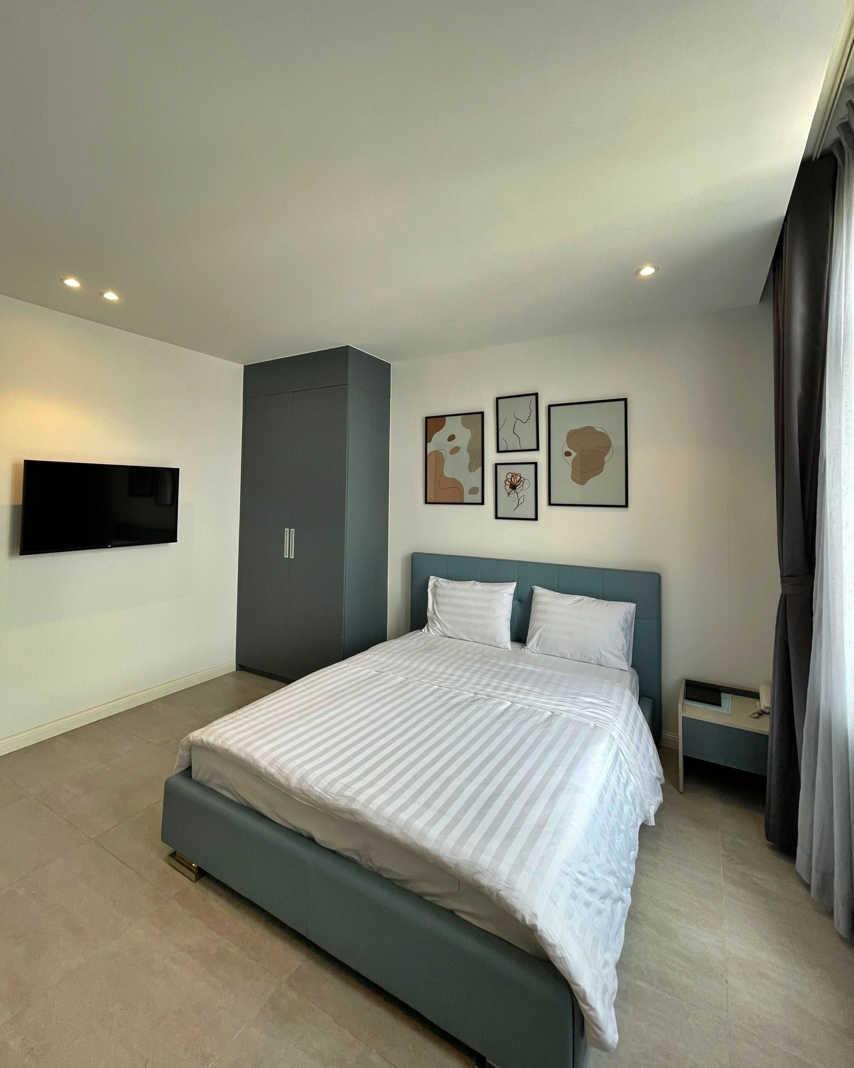 A modern bedroom with a large bed, a flat-screen TV mounted on the wall, and a grey wardrobe.