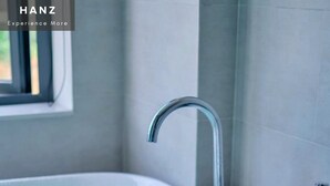 Una bañera con varios grifos, agua corriente y pétalos de rosa flotando en la superficie.