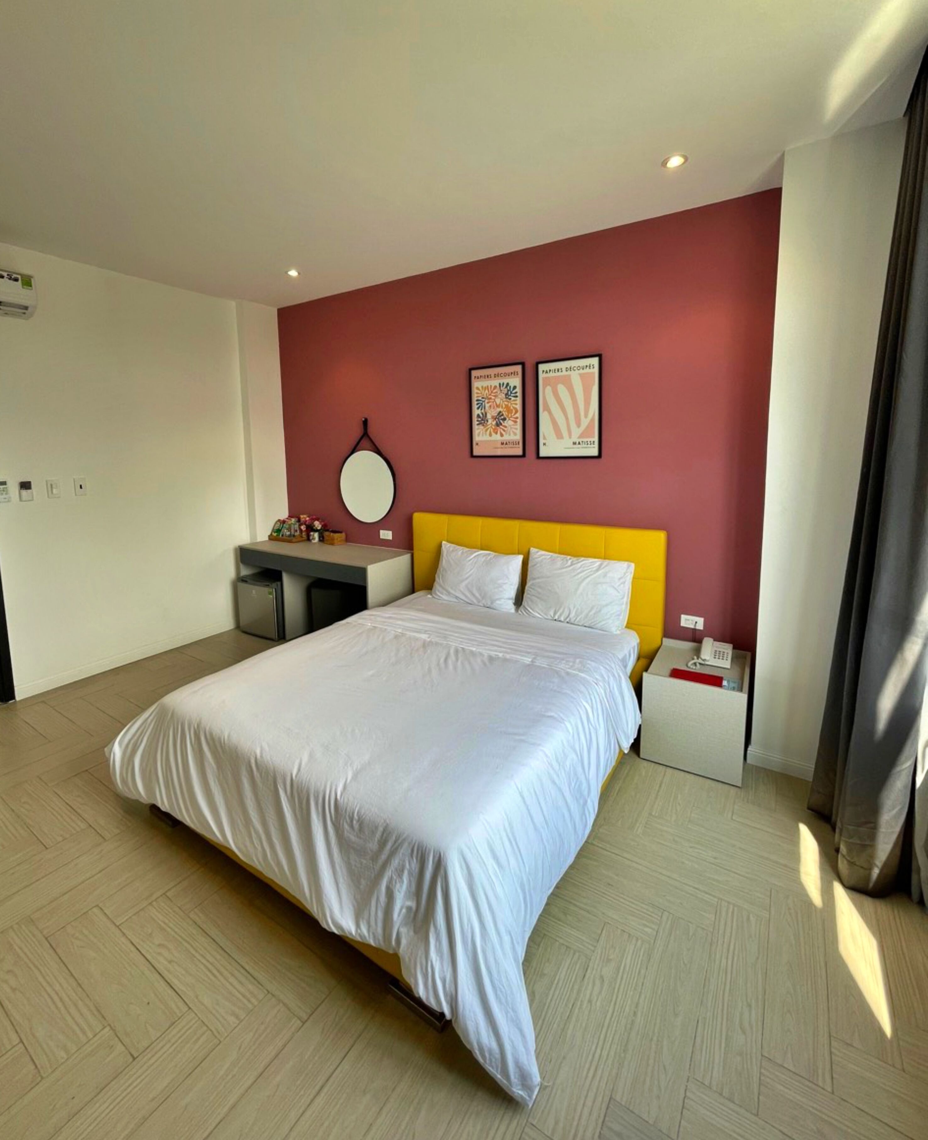 A hotel room with a bed, a desk, a chair, a mirror, and two framed artworks on the wall.
