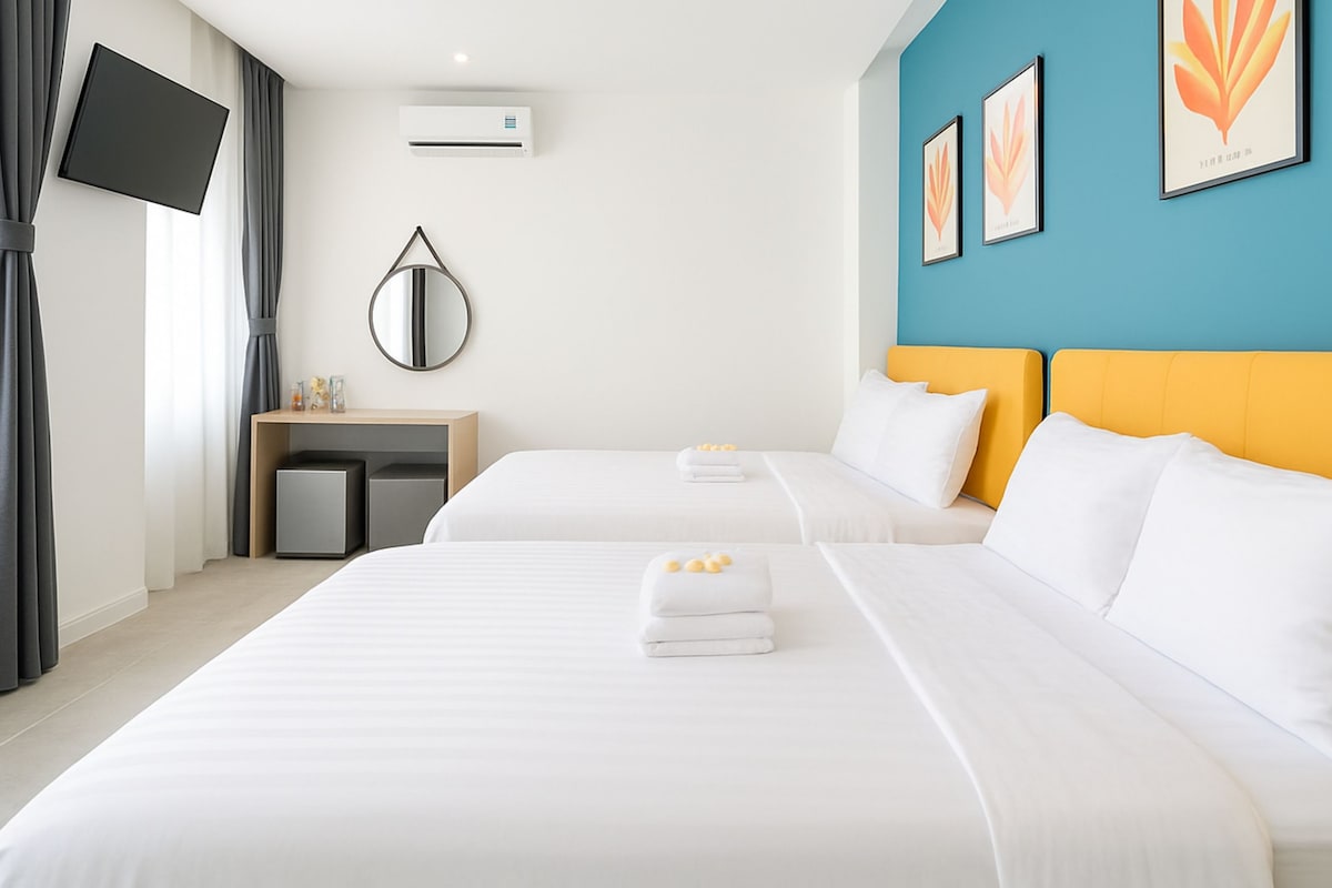 Hotellihuone, jossa on kaksi sänkyä, televisio, työpöytä ja taideteoksia seinillä.