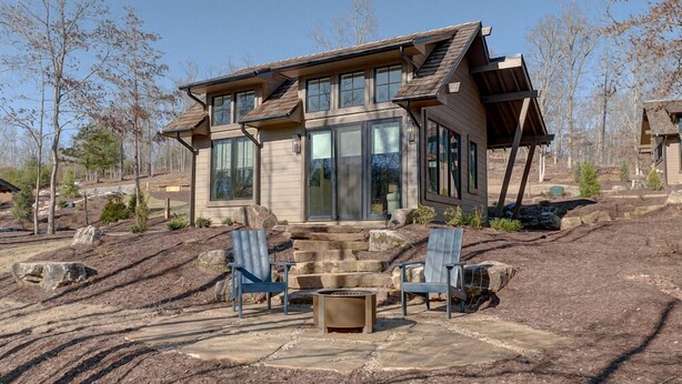 A modern house with a stone fireplace, two blue Adirondack chairs, and a stone patio. - Golf and Riverfront Cottage | King Bed | Group Availability (Mineral Bluff)