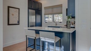 A kitchen with a large island, two bar stools, dark blue cabinets, and a window with a view. - Golf and Riverfront Cottage | King Bed | Group Availability (Mineral Bluff)