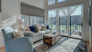 A spacious living room with a large window, a sofa, a chair, and a coffee table. - Golf and Riverfront Cottage | King Bed | Group Availability (Mineral Bluff)