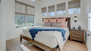 A bedroom with a large bed, a nightstand, a dresser, and a window with blinds. - Golf and Riverfront Cottage | King Bed | Group Availability (Mineral Bluff)