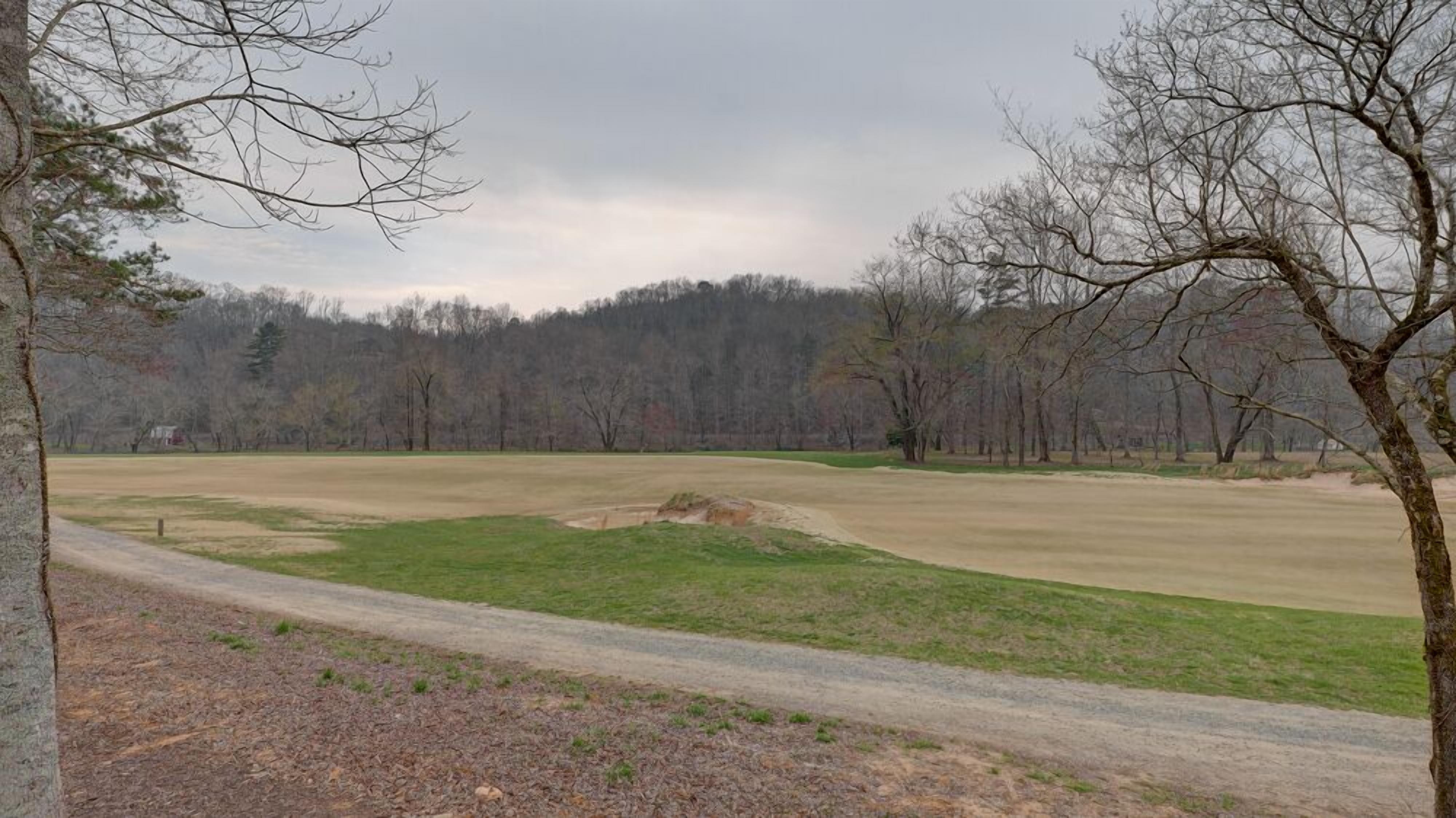 Ein Golfplatz mit einem Feldweg, Rasenflächen und einem Wald im Hintergrund.