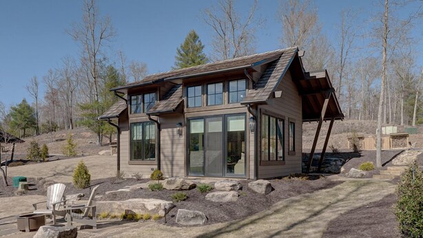 Een modern huis met twee verdiepingen, grote ramen en een schuin dak, omgeven door een aangelegde tuin met stenen en weinig beplanting.