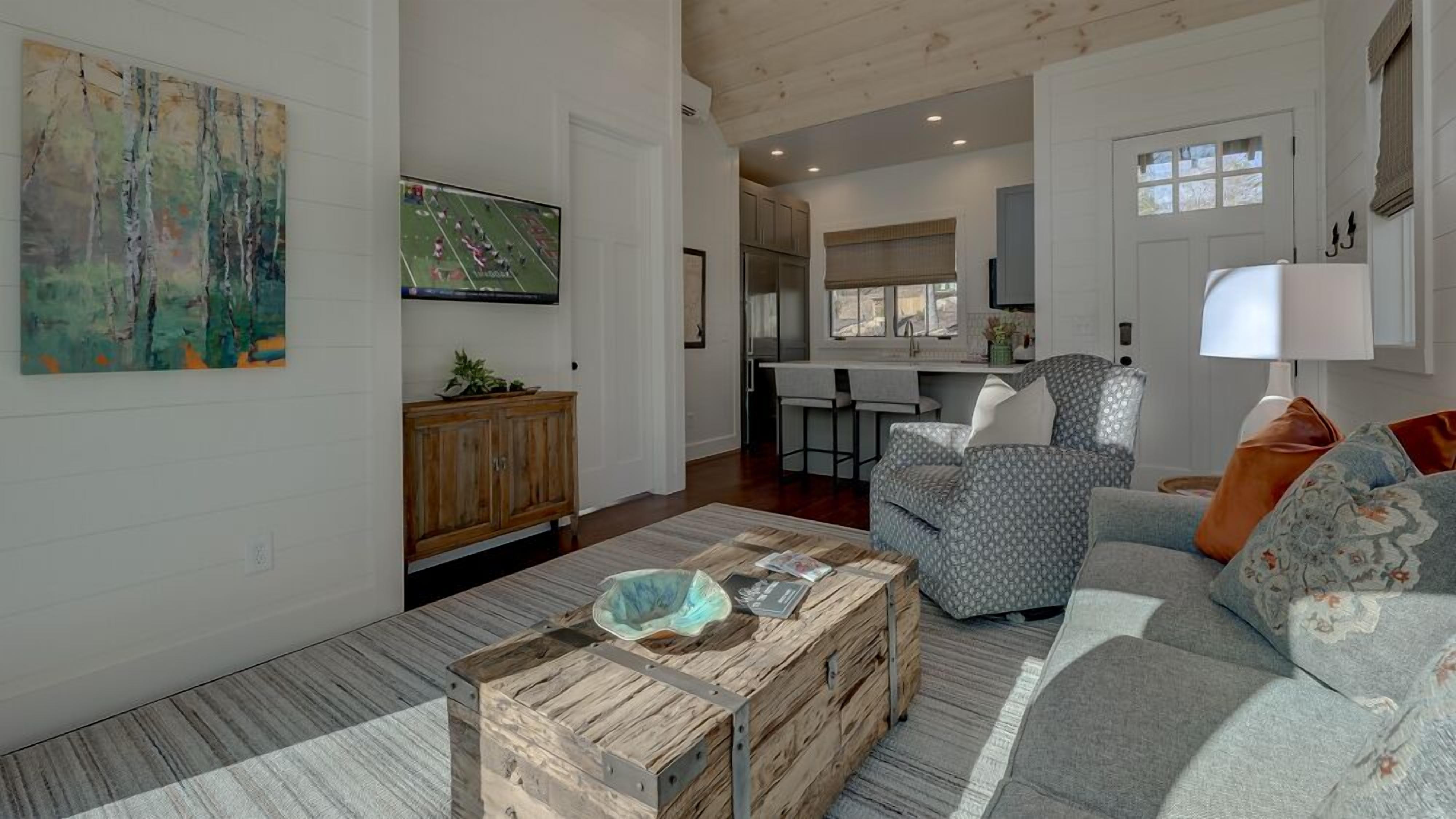 A spacious living room with a wooden coffee table, a grey patterned sofa, and a painting on the wall.