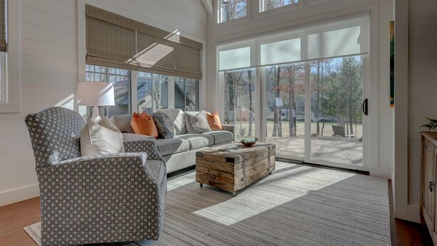Un salon spacieux avec un fauteuil à motifs gris, un canapé gris agrémenté de coussins orange et blancs, et une table basse en bois.