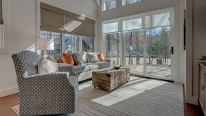 A spacious living room with a grey patterned armchair, a grey sofa with orange and white cushions, and a wooden coffee table.