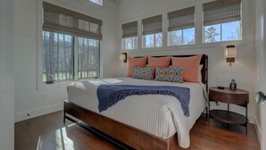 Une chambre à coucher avec un grand lit, de nombreuses fenêtres, une table de chevet avec un téléphone et une commode.