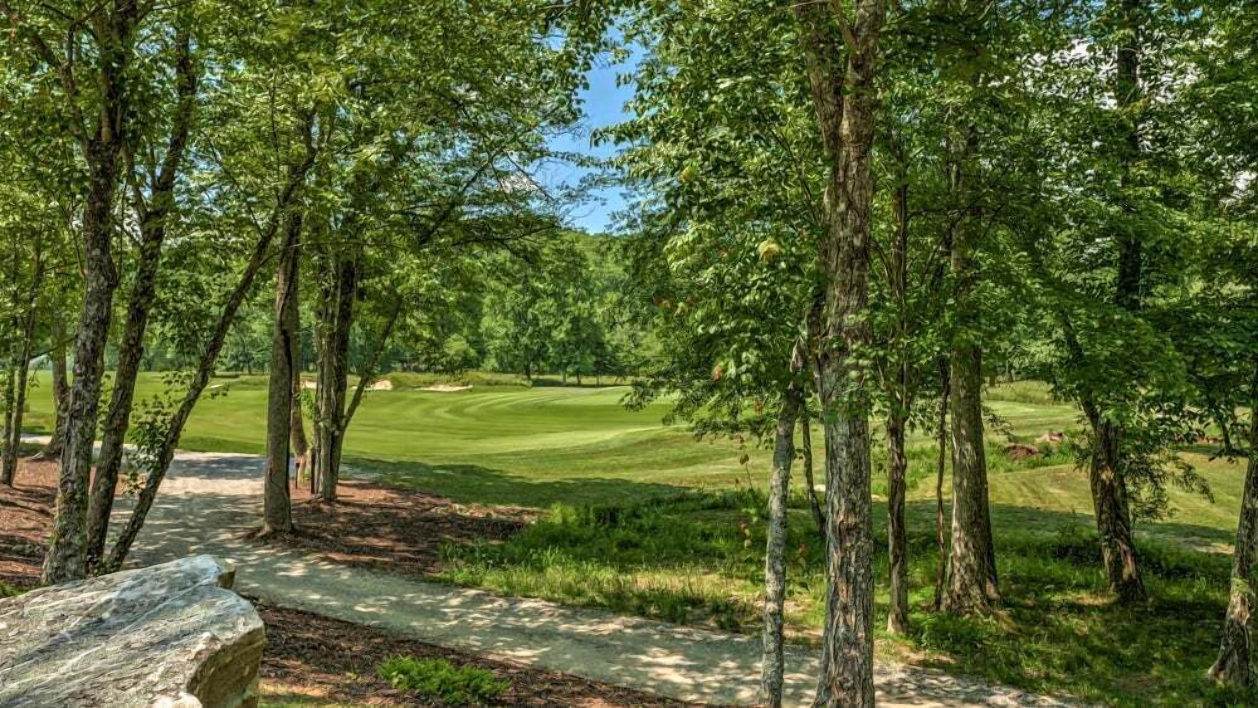 En golfbana med en stenlagd gångstig som leder genom ett skogsområde.