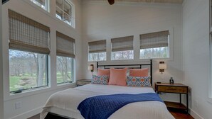 A bedroom with a large bed, multiple windows with blinds, a nightstand, and a lamp. - Golf and Riverfront Cottage | King Bed | Group Availability (Mineral Bluff)