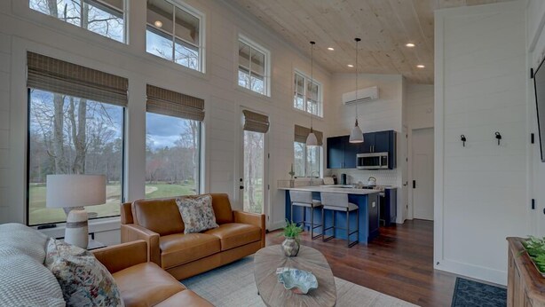 A spacious living area with a large window, a sofa, a coffee table, and a kitchen area with a bar. - Golf and Riverfront Cottage | King Bed | Group Availability (Mineral Bluff)