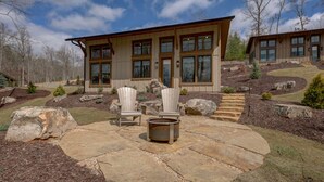 A modern two-story house with a stone patio, outdoor seating, and a fire pit. - Golf and Riverfront Cottage | King Bed | Group Availability (Mineral Bluff)