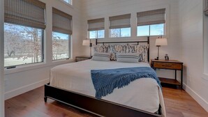 Une chambre avec un grand lit, de nombreuses fenêtres et une vue sur les arbres.