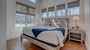 A bedroom with a large bed, multiple windows, and a bedside table with a lamp and phone. - Golf and Riverfront Cottage | King Bed | Group Availability (Blue Ridge)