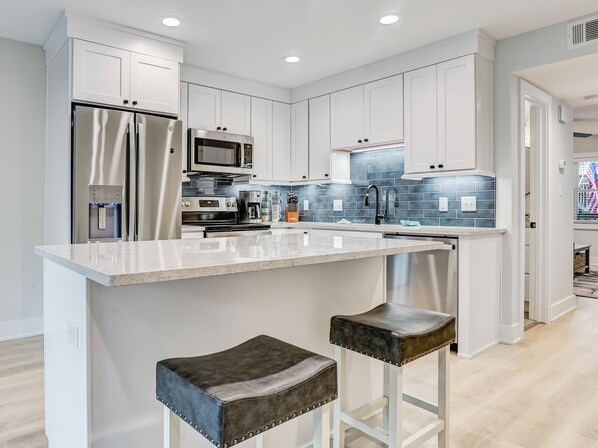 A modern kitchen with white cabinetry, stainless steel appliances, a marble countertop, and two stools.
