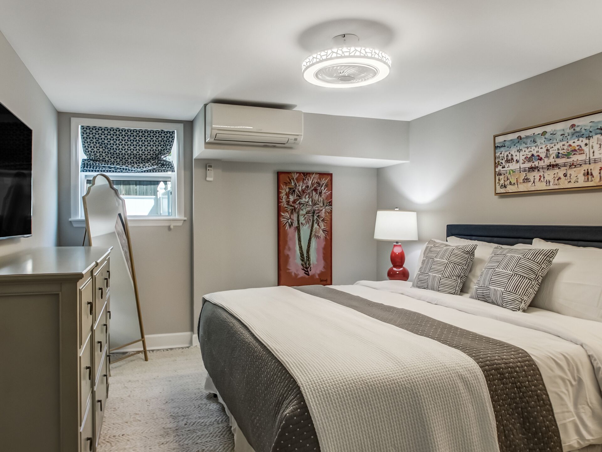 Een moderne slaapkamer met een bed, een bureau, een stoel, een airconditioner, een raam met een decoratief zonnescherm, een schilderij, een lamp en een plafondarmatuur.