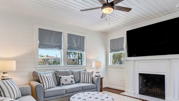 Sala de estar con sofá gris, reposapiés y cojines estampados, chimenea y ventilador de techo.