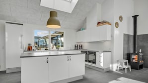A modern kitchen with a large island, white cabinetry, and a wood-burning stove. - Nice home in Bogense with sauna (Bogense)